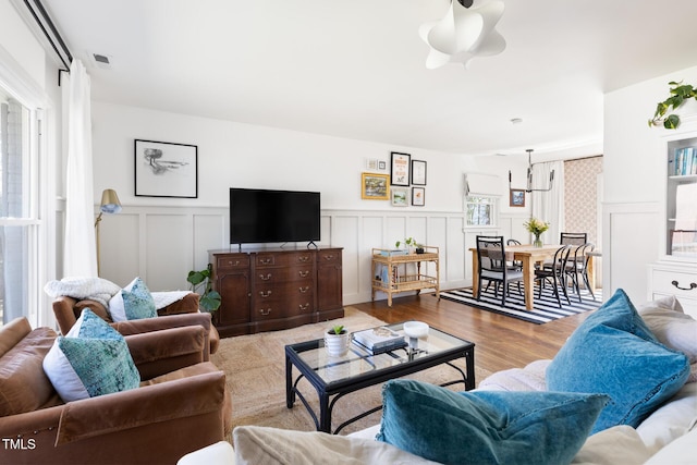 living area with a wainscoted wall, wood finished floors, visible vents, and a decorative wall