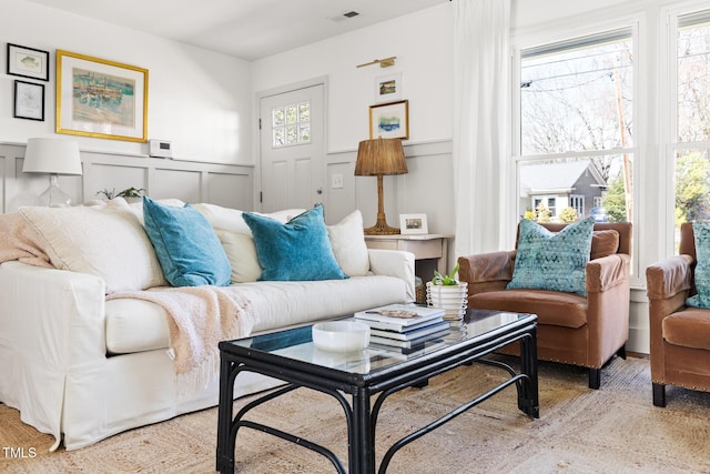 living room featuring visible vents, a decorative wall, and wainscoting