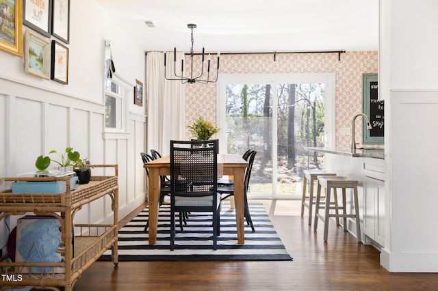 dining space featuring dark wood-style floors, a wainscoted wall, an inviting chandelier, and a decorative wall