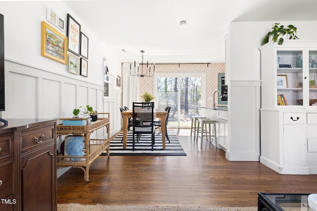 dining space featuring dark wood-style floors, wainscoting, a decorative wall, and an inviting chandelier