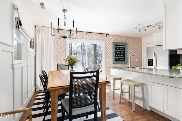 dining space with wallpapered walls, visible vents, dark wood finished floors, rail lighting, and a notable chandelier