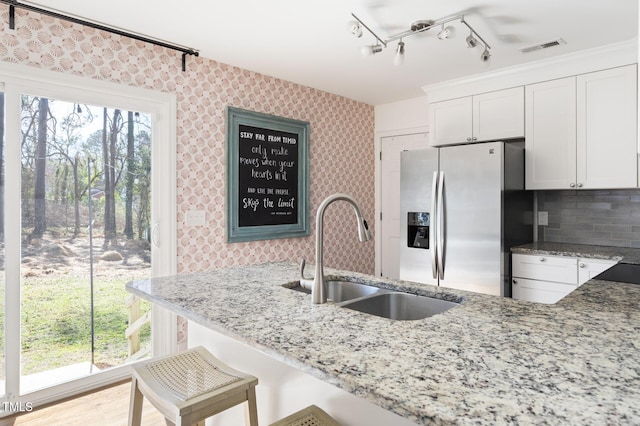 kitchen featuring light stone countertops, a sink, stainless steel refrigerator with ice dispenser, and wallpapered walls