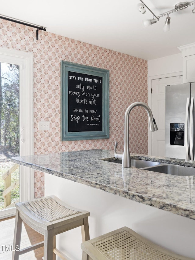 kitchen featuring light stone countertops, wallpapered walls, a sink, and stainless steel fridge with ice dispenser