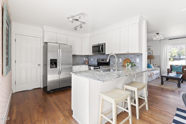 kitchen with a peninsula, appliances with stainless steel finishes, white cabinets, and light stone counters