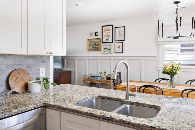 kitchen with tasteful backsplash, dishwasher, light stone countertops, white cabinetry, and a sink