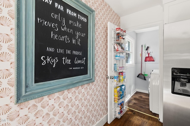 interior space with dark wood-type flooring, baseboards, stainless steel refrigerator with ice dispenser, washer / dryer, and wallpapered walls