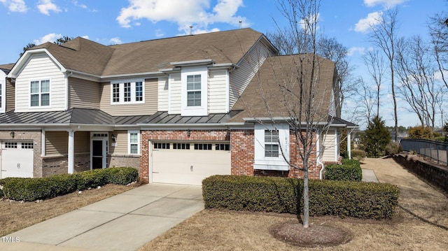 view of property featuring metal roof, an attached garage, brick siding, driveway, and a standing seam roof