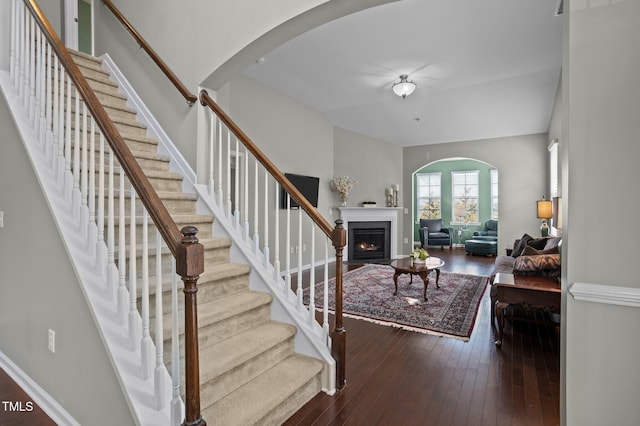 interior space with hardwood / wood-style flooring, a fireplace with flush hearth, arched walkways, and baseboards