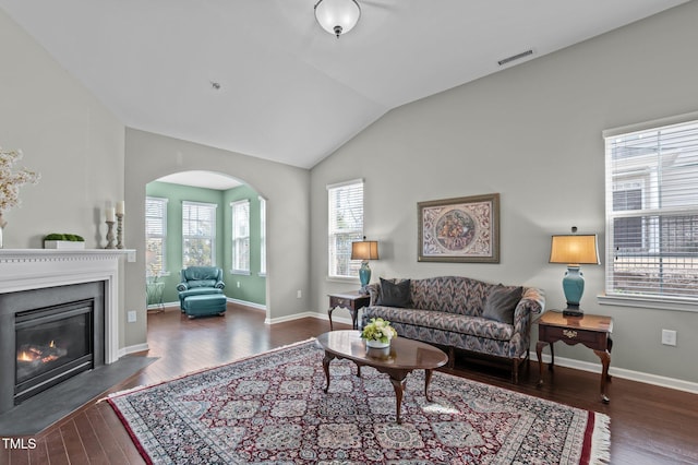 living area featuring arched walkways, lofted ceiling, visible vents, a fireplace with flush hearth, and wood finished floors