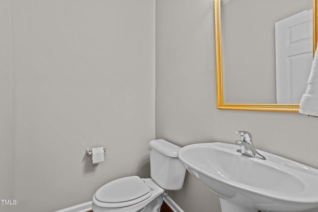 half bath featuring toilet, baseboards, and a sink