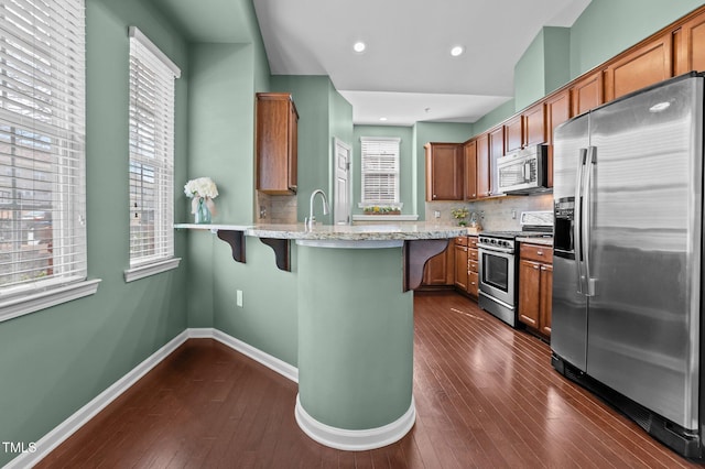 kitchen with baseboards, appliances with stainless steel finishes, a kitchen breakfast bar, light stone counters, and a peninsula