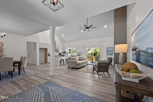 living area with ceiling fan with notable chandelier, high vaulted ceiling, light wood finished floors, and decorative columns