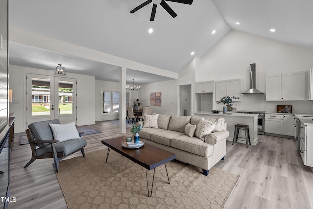 living room featuring ceiling fan with notable chandelier, french doors, light wood finished floors, and high vaulted ceiling