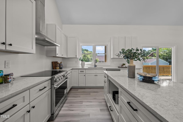 kitchen featuring white cabinets, wall chimney exhaust hood, light wood-style flooring, high end stainless steel range oven, and a sink