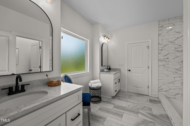 full bath featuring marble finish floor, two vanities, a sink, and a tile shower