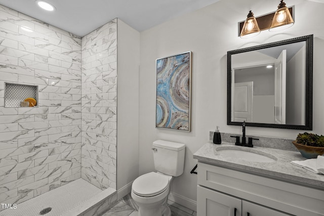 bathroom featuring marble finish floor, toilet, vanity, tiled shower, and baseboards