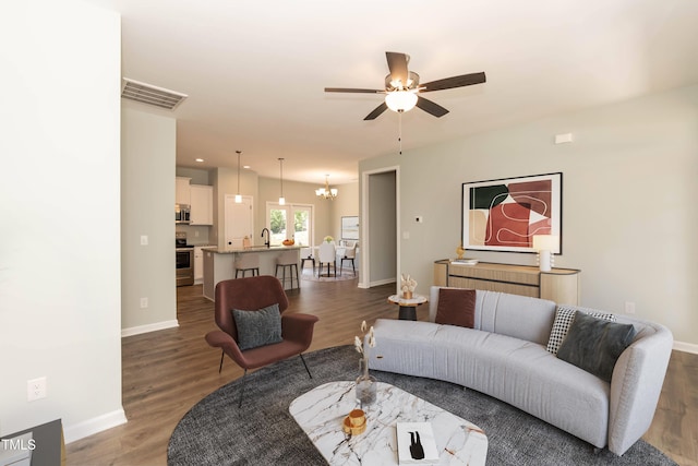 living room with baseboards, visible vents, wood finished floors, and ceiling fan with notable chandelier