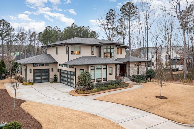 prairie-style home featuring stone siding, a shingled roof, an attached garage, and driveway