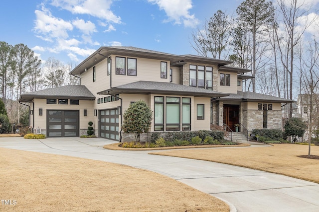 prairie-style home featuring a shingled roof, stone siding, an attached garage, and concrete driveway