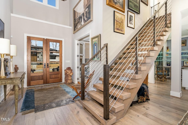 foyer entrance with french doors, stairway, wood finished floors, and a towering ceiling