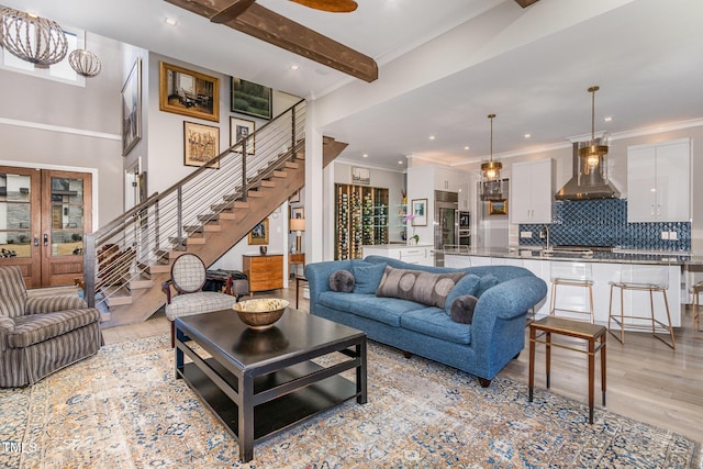 living area featuring light wood-style floors, ornamental molding, french doors, stairway, and beamed ceiling