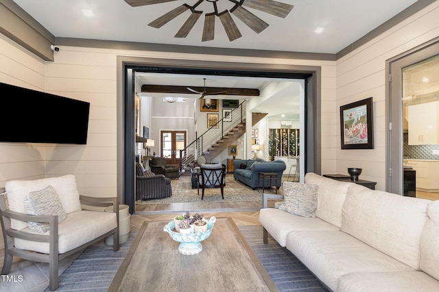 living area with wood walls, ceiling fan, and stairs