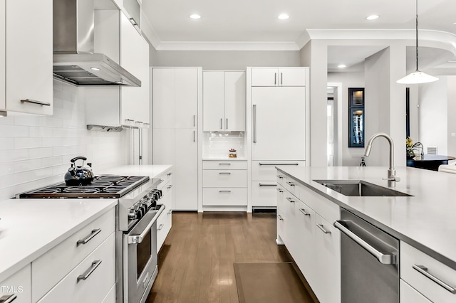 kitchen with stainless steel appliances, light countertops, a sink, wall chimney range hood, and modern cabinets