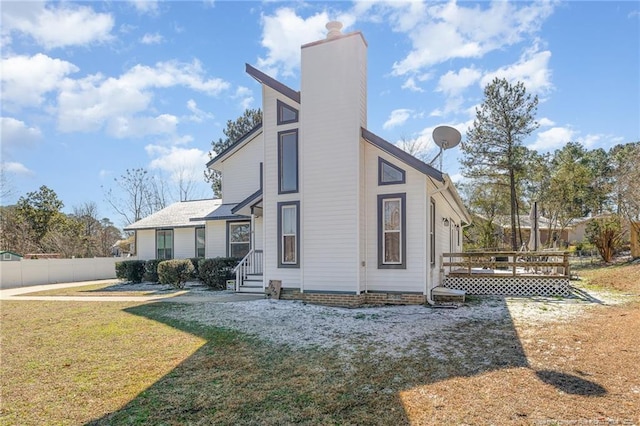 view of property exterior featuring a chimney, a lawn, entry steps, fence, and a wooden deck