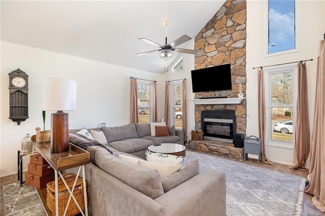 living room with baseboards, ceiling fan, wood finished floors, a stone fireplace, and high vaulted ceiling