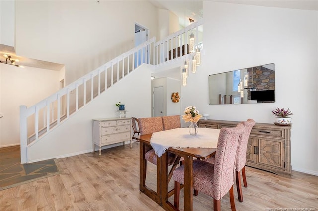 dining room with a towering ceiling, light wood-style flooring, stairway, and baseboards