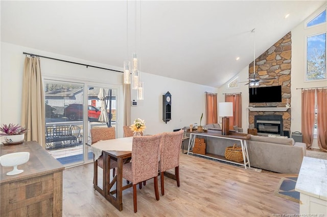 dining area featuring light wood-type flooring, ceiling fan, a fireplace, and high vaulted ceiling