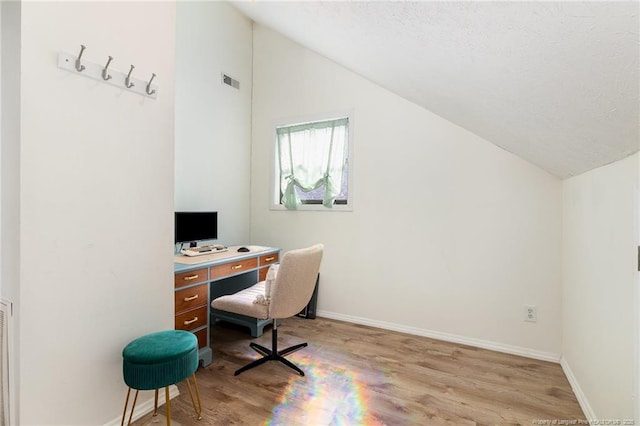 office area featuring vaulted ceiling, light wood-type flooring, visible vents, and baseboards