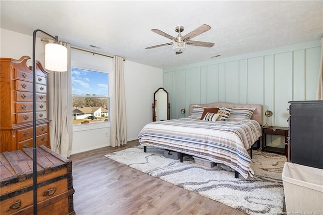 bedroom with a ceiling fan, visible vents, a decorative wall, and wood finished floors