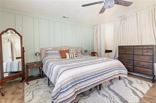 bedroom with visible vents, a decorative wall, a ceiling fan, connected bathroom, and wood finished floors