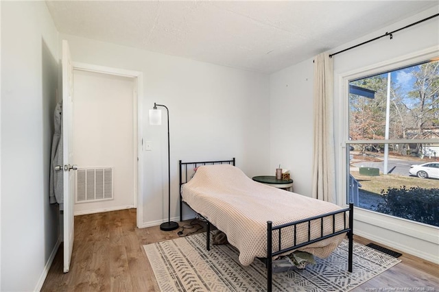 bedroom with baseboards, visible vents, and wood finished floors