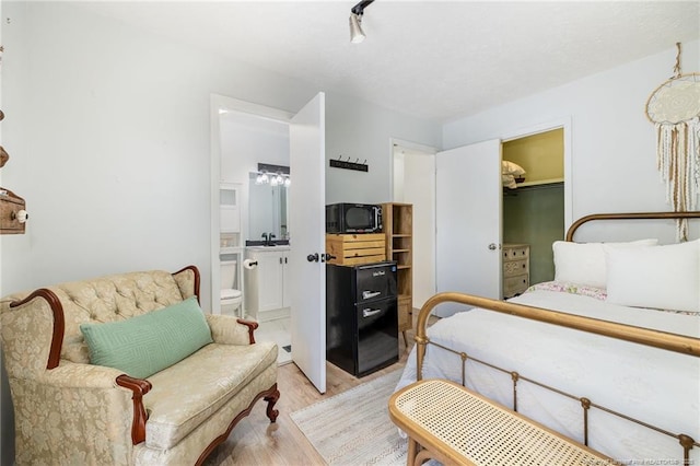 bedroom featuring ensuite bath, light wood-style flooring, a walk in closet, and a sink