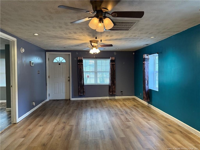 foyer entrance with a textured ceiling, wood finished floors, visible vents, and baseboards