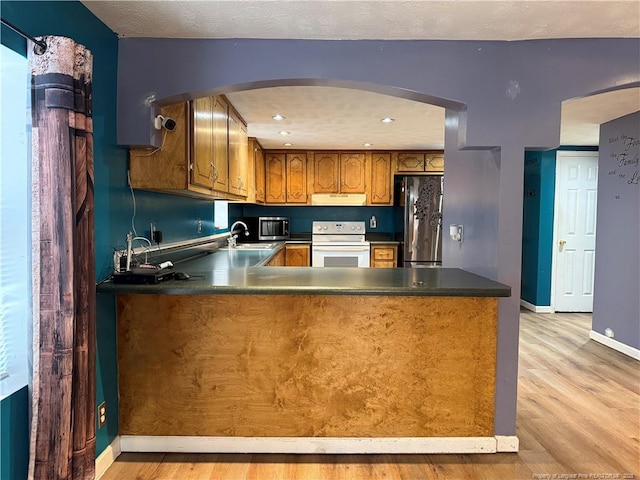 kitchen with under cabinet range hood, a peninsula, a sink, appliances with stainless steel finishes, and brown cabinetry