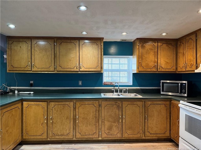 kitchen with brown cabinets, stainless steel microwave, white range with electric cooktop, and a sink