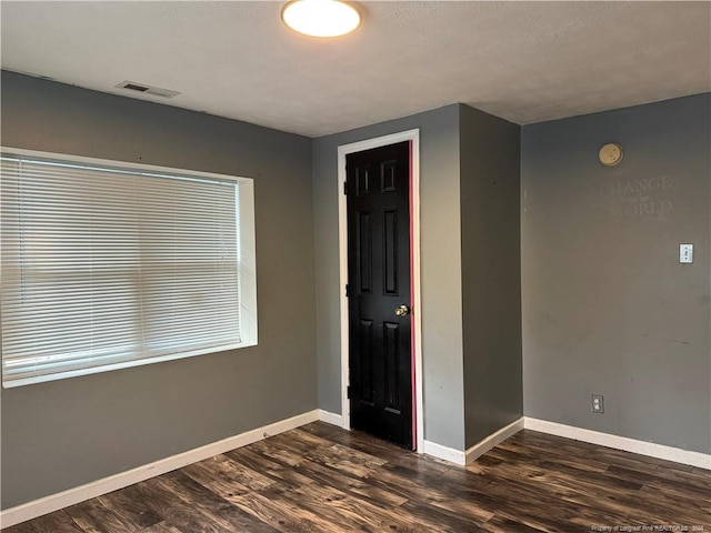 empty room with dark wood-style floors, baseboards, and visible vents