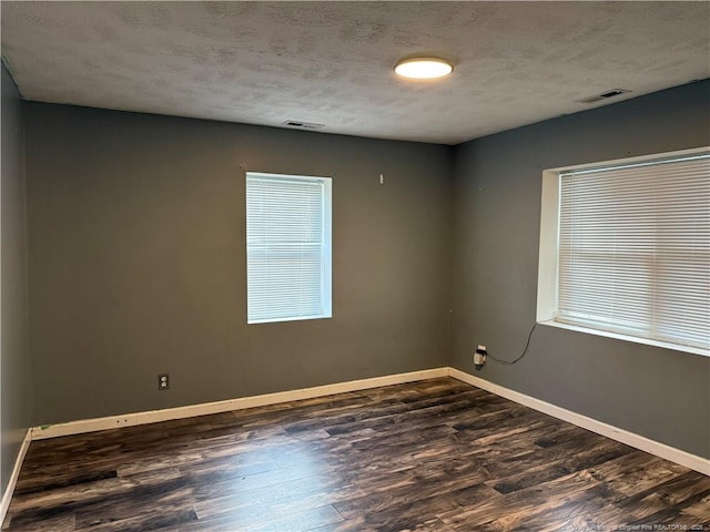 spare room featuring a textured ceiling, dark wood-style flooring, visible vents, and baseboards