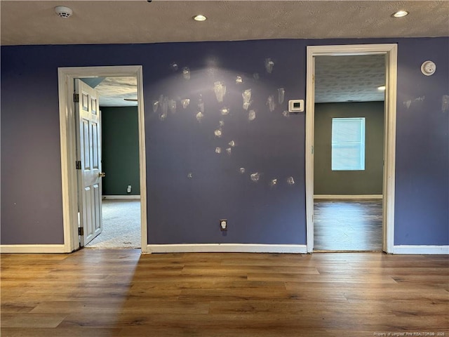 empty room featuring a textured ceiling, baseboards, and wood finished floors