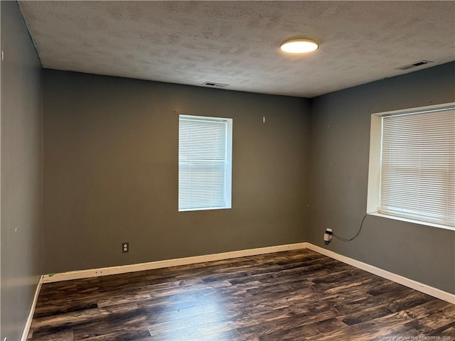 empty room featuring dark wood-style floors, baseboards, and visible vents