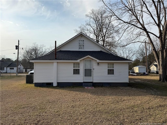 back of property with entry steps, crawl space, roof with shingles, and a yard