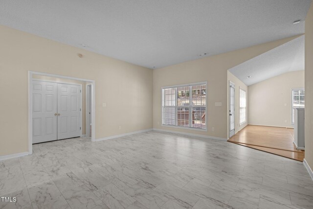 spare room with lofted ceiling, marble finish floor, baseboards, and a textured ceiling