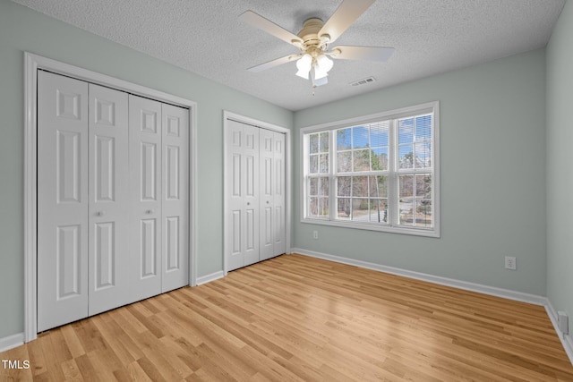 unfurnished bedroom featuring a textured ceiling, two closets, light wood-style flooring, and baseboards