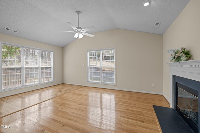 unfurnished living room with visible vents, lofted ceiling, a fireplace with flush hearth, light wood-style flooring, and a healthy amount of sunlight