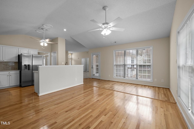 unfurnished living room with baseboards, lofted ceiling, ceiling fan, a textured ceiling, and light wood-type flooring