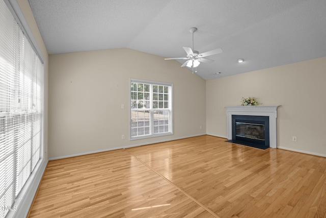 unfurnished living room featuring lofted ceiling, ceiling fan, a fireplace with flush hearth, light wood-style flooring, and a textured ceiling