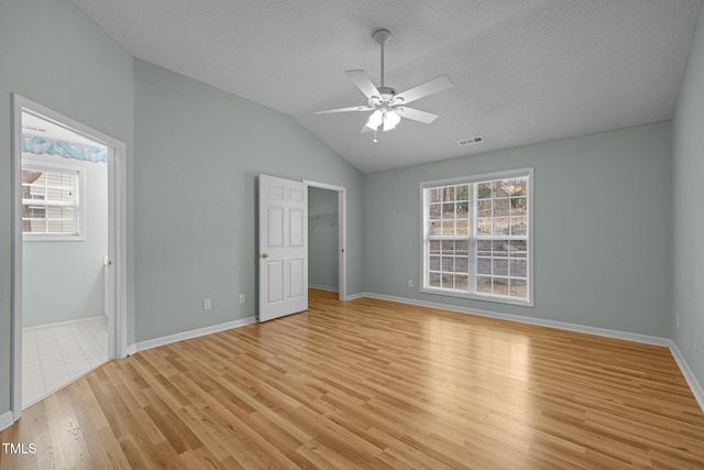 unfurnished bedroom featuring light wood finished floors, lofted ceiling, visible vents, a spacious closet, and baseboards